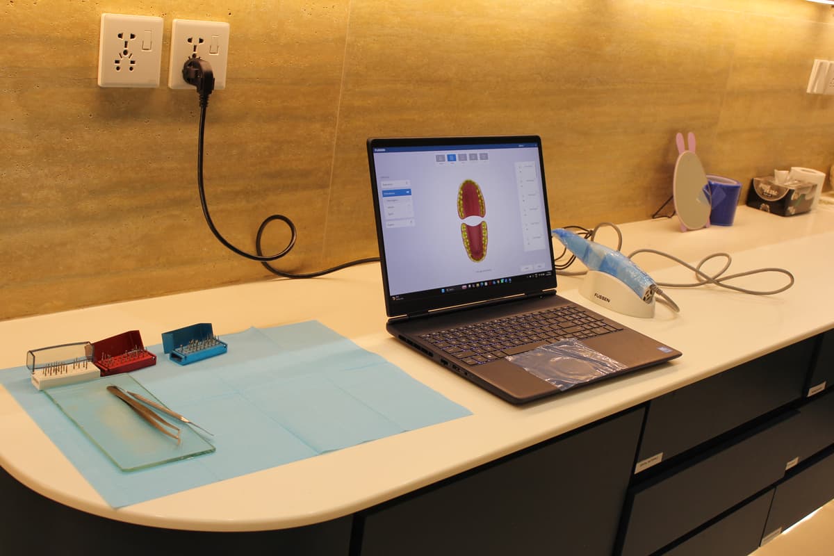Intraoral digital scanner with 3D dental scan displayed on laptop